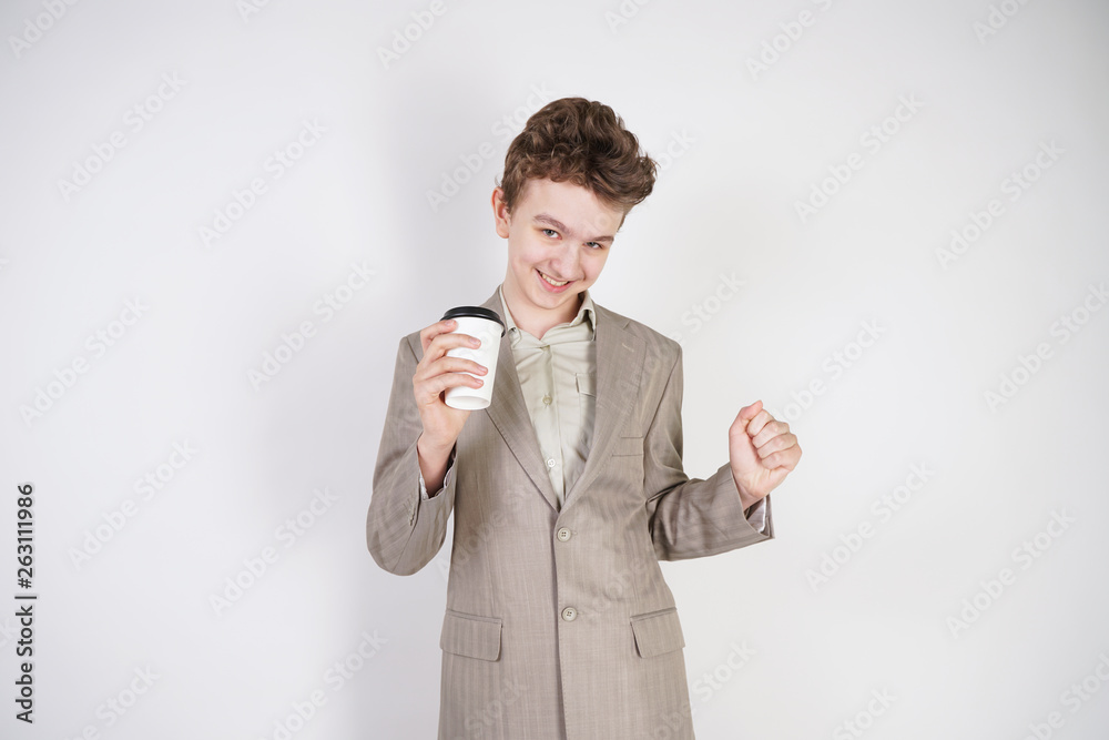 Wall mural young caucasian man in a business suit with a cup of drink in his hand is glad of his success on a w