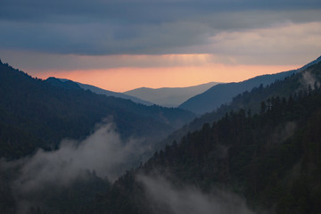 Fototapeta premium Zachód słońca za warstwowymi górami pod dramatycznym krajobrazem chmur w Parku Narodowym Great Smoky Mountains w stanie Tennessee wczesnym latem.