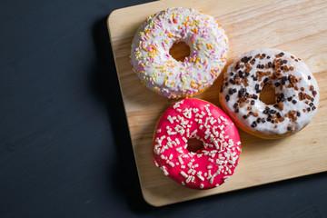 White, pink and brown glazed donuts on black wooden background.