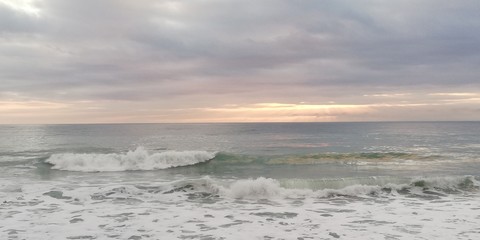 Fototapeta na wymiar Sunset seascape. Autumn storm sea. Gray, blue, turquoise waves with white foam break on a rocky beach. The sun breaks through the low heavy clouds. Background