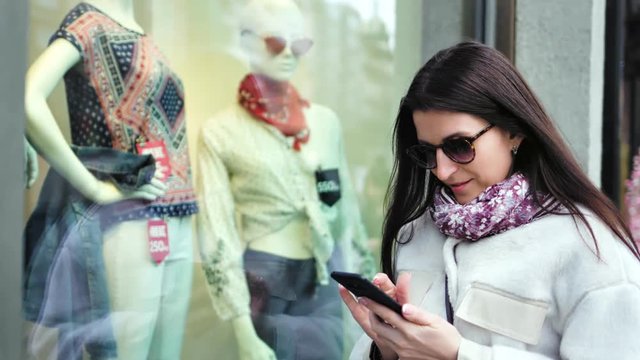 Stylish shopper woman taking photo of dummy in showcase of shop fashion clothes using smartphone