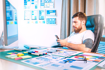 graphic designer testing the application on the phone. Design for mobile devices. Office of the designer. A man works at a computer.