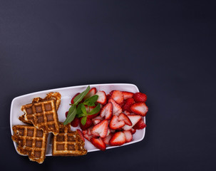 Freshly baked gluten free waffles with strawberries on mint  on a rectangular dish..