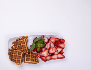Freshly baked gluten free waffles with strawberries on mint  on a rectangular dish..