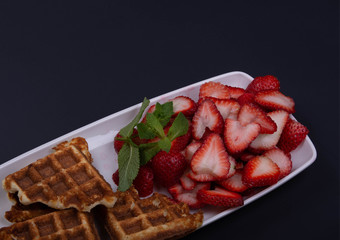 Freshly baked gluten free waffles with strawberries on mint  on a rectangular dish..