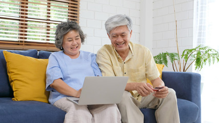 Senior asian couple shopping online by using laptop computer and credit card at home living room, Retirement people technology lifestyle