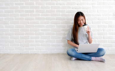 Young asian woman using laptop computer and holding coffee cup in casual style at white room background with copy space, people and technology, lifestyles