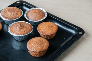 Fresh cupcakes are on a black pan on the table