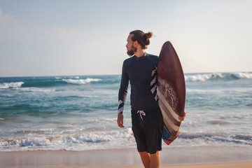 Young attractive sporty stylish man with a surfboard in his hands against the background of the ocean beach,sport freedom vacation travel concept