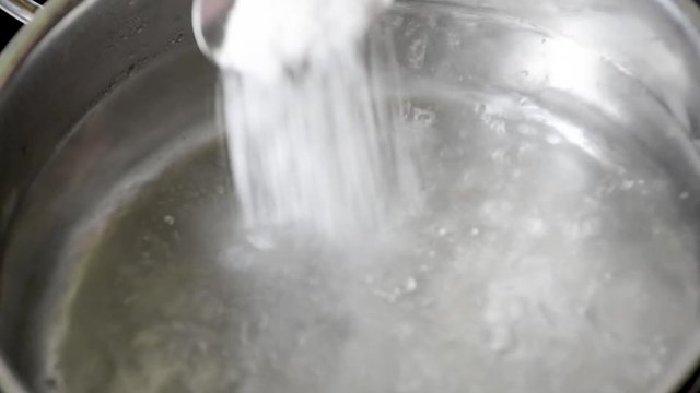 Add salt to boiling water, cook soup or other cooking options Salt pour into a pot of water in natural light 