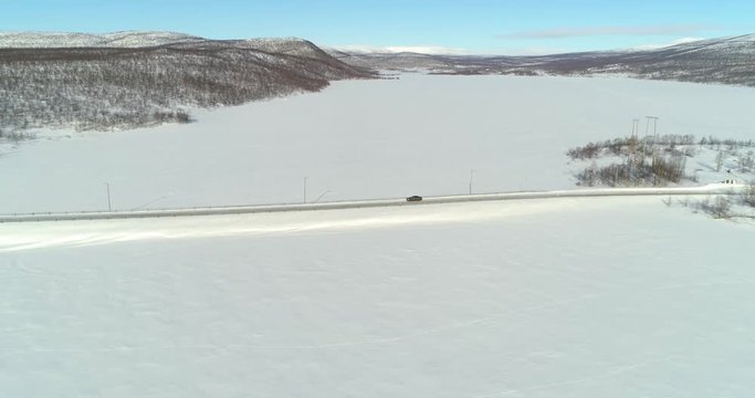 Aerial, drone shot, of a car on route e8, between frozen polar lake and boreal wilderness, in Kasivarren eramaa, Enontekio, Lapland, Finland