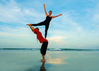 Fototapeta premium healthy and attractive fit couple of acrobats doing acroyoga balance and meditation exercise on beautiful desert beach practicing balance and harmony posing