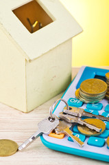 stacking coins and bunch of key on calculator with house replica on wooden desk for home loans concept