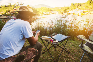 Asian men are using the phone to search for tourist information, Travel nature, Travel relax, Concept of Camping Relaxing Tourism in village Countryside.