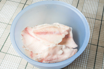 Frozen tilapia fish in deep defrosting bowl.