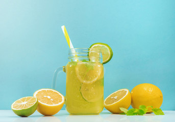 Lemonade drink of soda water, citrus and mint on the light blue background. Cocktail glass with handle and straw, sliced lemon and lime, front view