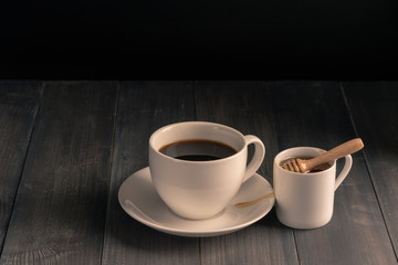 Coffee cup and sweet honey on black wooden background.
