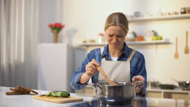 Girl disgusted with stinky meal on stove, spoiled ingredients, untasty food