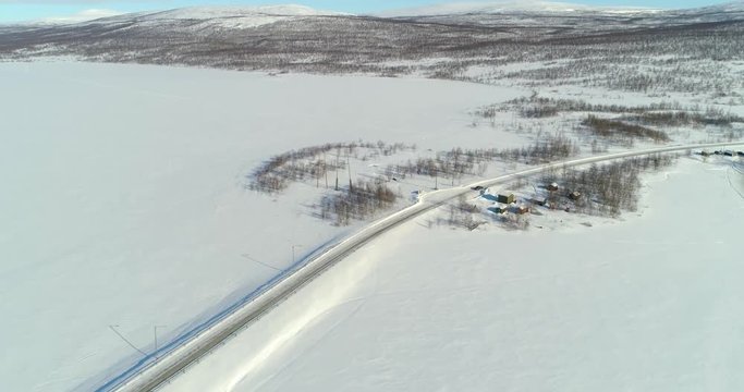 Aerial, drone shot, of a car on route e8, between frozen polar lake and boreal wilderness, in Kasivarren eramaa, Enontekio, Lapland, Finland