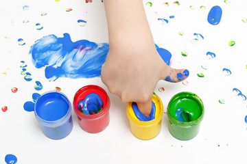 A child draws with colorful paint with his fingers on white paper.