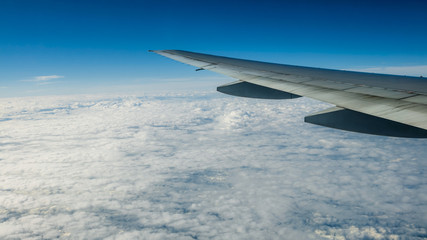 Close up of window with airplane wing. Beautiful cloudscape with clear blue sky.