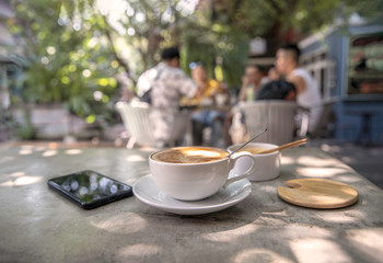 Coffee cup , mobile phone and sugar cup on stone table with sunlight in garden background