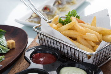French fries in stainless basket on glass table.