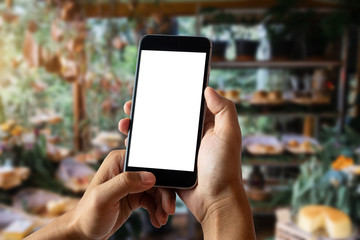 Hands holding a white mobile phone with a blank white screen in the corner of the Bakery shop.