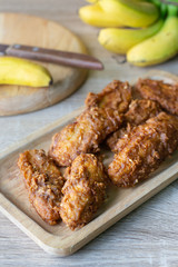 Deep fried banana in wooden dish with banana on table.
