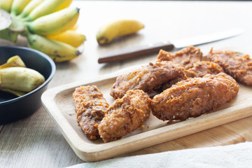 Deep fried banana in wooden dish with banana on table.