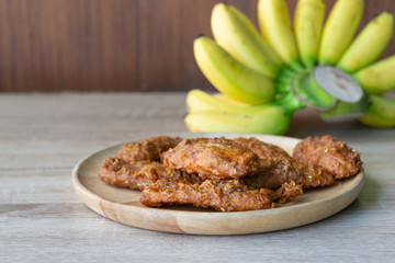 Deep fried banana in wooden dish with banana on table.