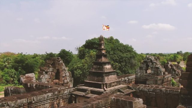 Aerial drone view ancient Asian temple in Cambodia; fly low and pull back from temple peak to reveal ruined walls of this historical Buddhist and Hindu structure.