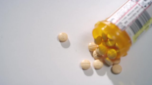 Macro close-up rack focus of a pill bottle of amphetamine / dextroamphetamine pills scattered on a white surface