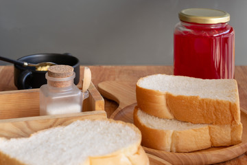 Slices bread in wooden dish with strawberry jam on wooden table.