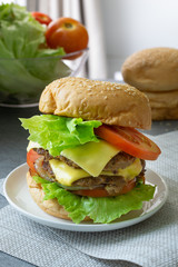 Hamburger with beef,cheese,lettuce,onion and tomato in white dish on concrete table.