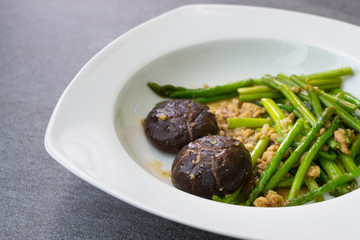 Fried asparagus and shiitake with oyster sauce in white dish on concrete table.