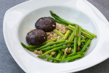 Fried asparagus and shiitake with oyster sauce in white dish on concrete table.