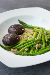 Fried asparagus and shiitake with oyster sauce in white dish on concrete table.