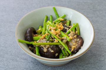 Fried asparagus and shiitake with oyster sauce in green bowl on concrete table.