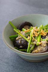 Fried asparagus and shiitake with oyster sauce in green bowl on concrete table.