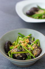Fried asparagus and shiitake with oyster sauce in green bowl on concrete table.