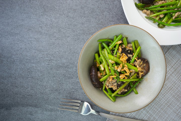 Fried asparagus and shiitake with oyster sauce in green bowl on concrete table.