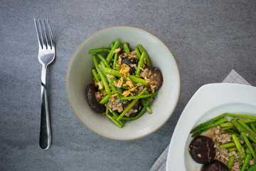 Fried asparagus and shiitake with oyster sauce in green bowl on concrete table.