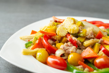 Stir fried vegetables with sweet pepper,tomato,pumpkin,corn and chicken in white dish on concrete table.