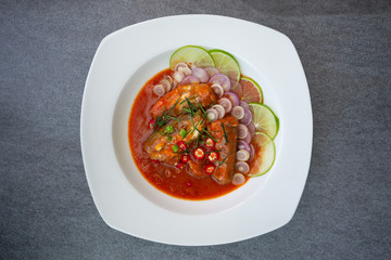 Spicy sardine salad with tomato sauce in white dish on concrete table.