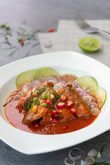 Spicy sardine salad with tomato sauce in white dish on concrete table.