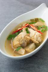 Sour and spicy soup with chicken drumstick in white bowl on concrete table.