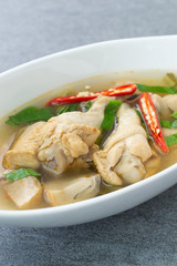 Sour and spicy soup with chicken drumstick in white bowl on concrete table.