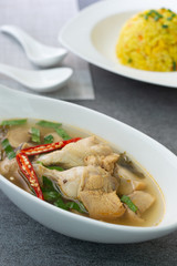 Sour and spicy soup with chicken drumstick and in white bowl and fried rice with turmeric in white dish on concrete table.