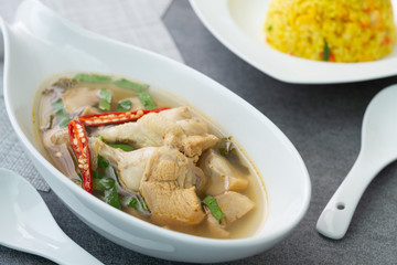 Sour and spicy soup with chicken drumstick and in white bowl and fried rice with turmeric in white dish on concrete table.